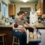 Mother holding baby and placing labeled breast milk bags in freezer drawer